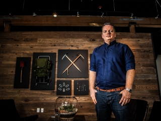 Ceo of Outdoor Equipment company stand in front of mounted equipment on wall